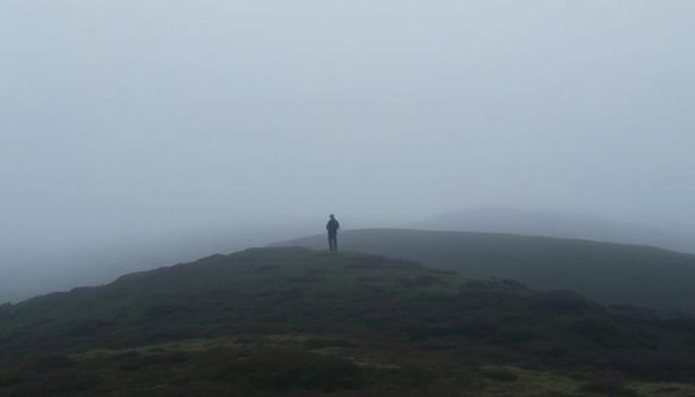 A lone hiker standing on a foggy hilltop
